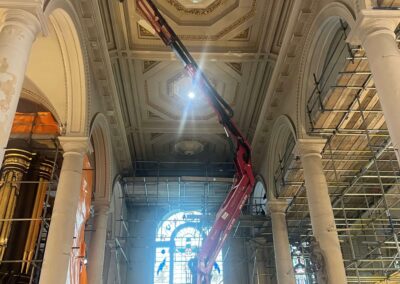 A mobile elevated work platform reaching the decorated lath and plaster ceiling of Holy Sepulchre London during conservation works by Cliveden Conservation, with scaffold towers visible to the sides of the nave.