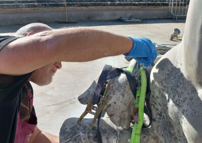 A Cliveden Conservation conservator carefully working on a marble sculptural element at the South Fountain at Waddesdon Manor using straps during conservation treatment